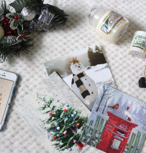A photo of christmas cards, two christmas yankee candles, a santa decoration, christmas flower decorations and an iphone with a photo of a quote in gold writing on white background that says 'It's the most wonderful time of the year'