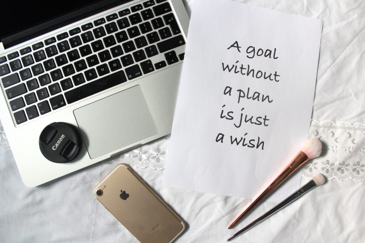 A photo of a macbook and iPhone with a printed quote next to them that says 'a goal without a plan is just a wish.'