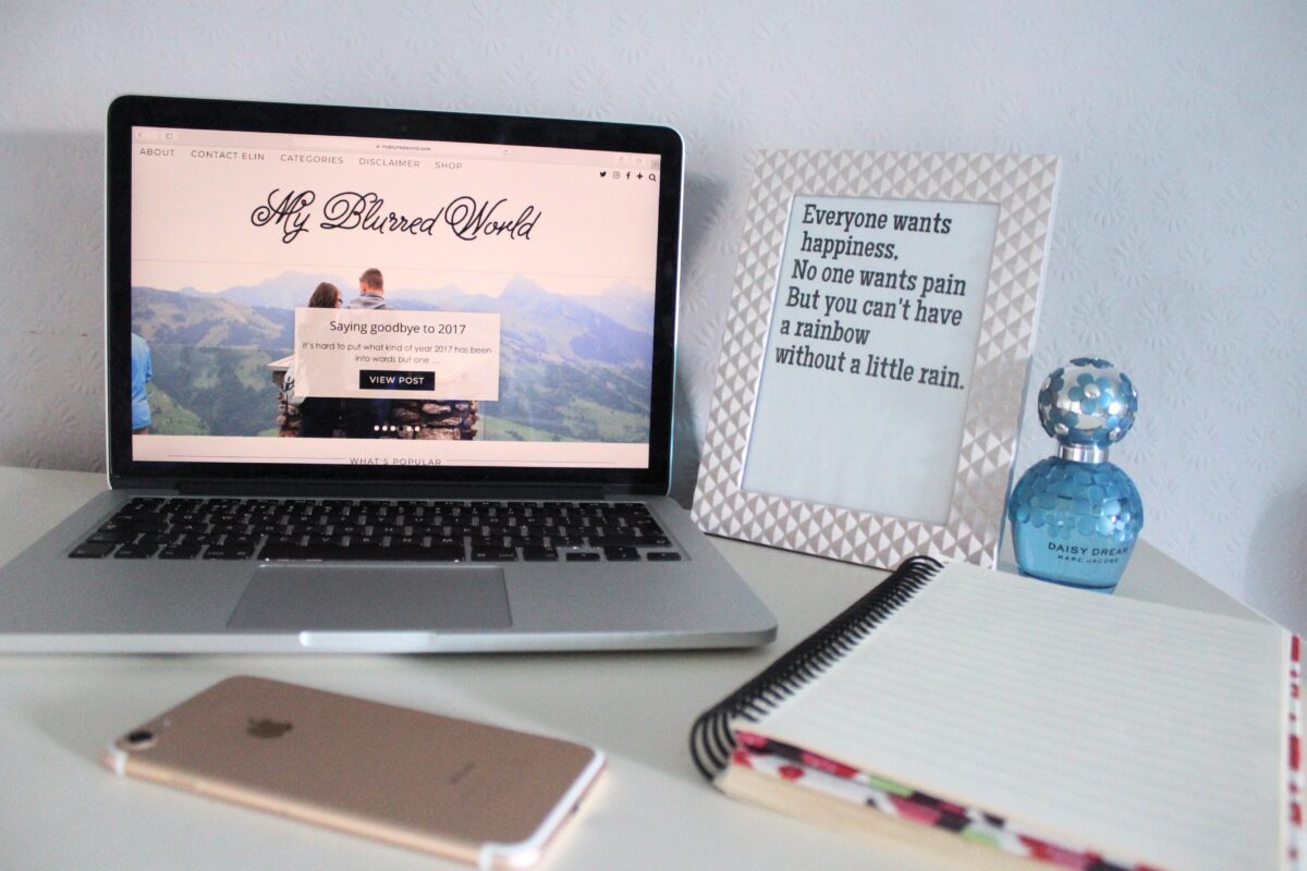 A photo of my blog on a macbook, there is a quote in a frame next to it that says everyone wants happiness, no one wants pain but you can't have a rainbow without a little rain