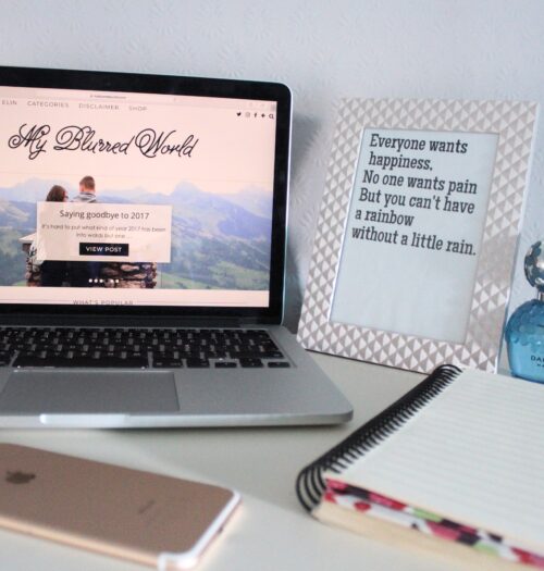 A photo of my blog on a macbook, there is a quote in a frame next to it that says everyone wants happiness, no one wants pain but you can't have a rainbow without a little rain