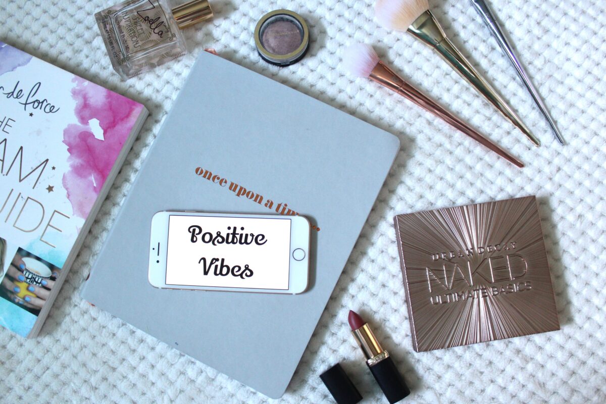 A photo of a quote on my phone that says 'positive vibes' and there are beauty products around it