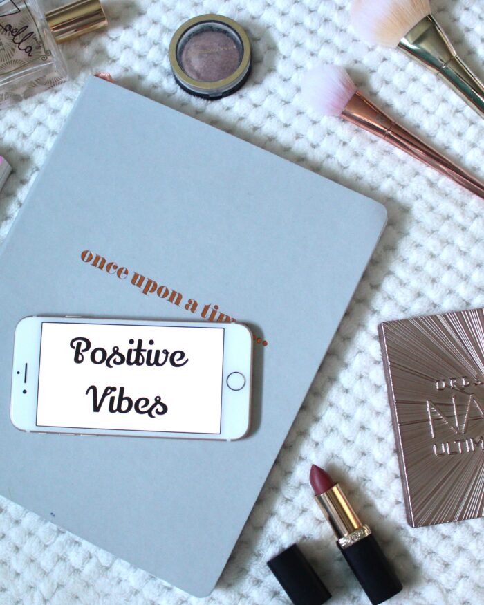 A photo of a quote on my phone that says 'positive vibes' and there are beauty products around it