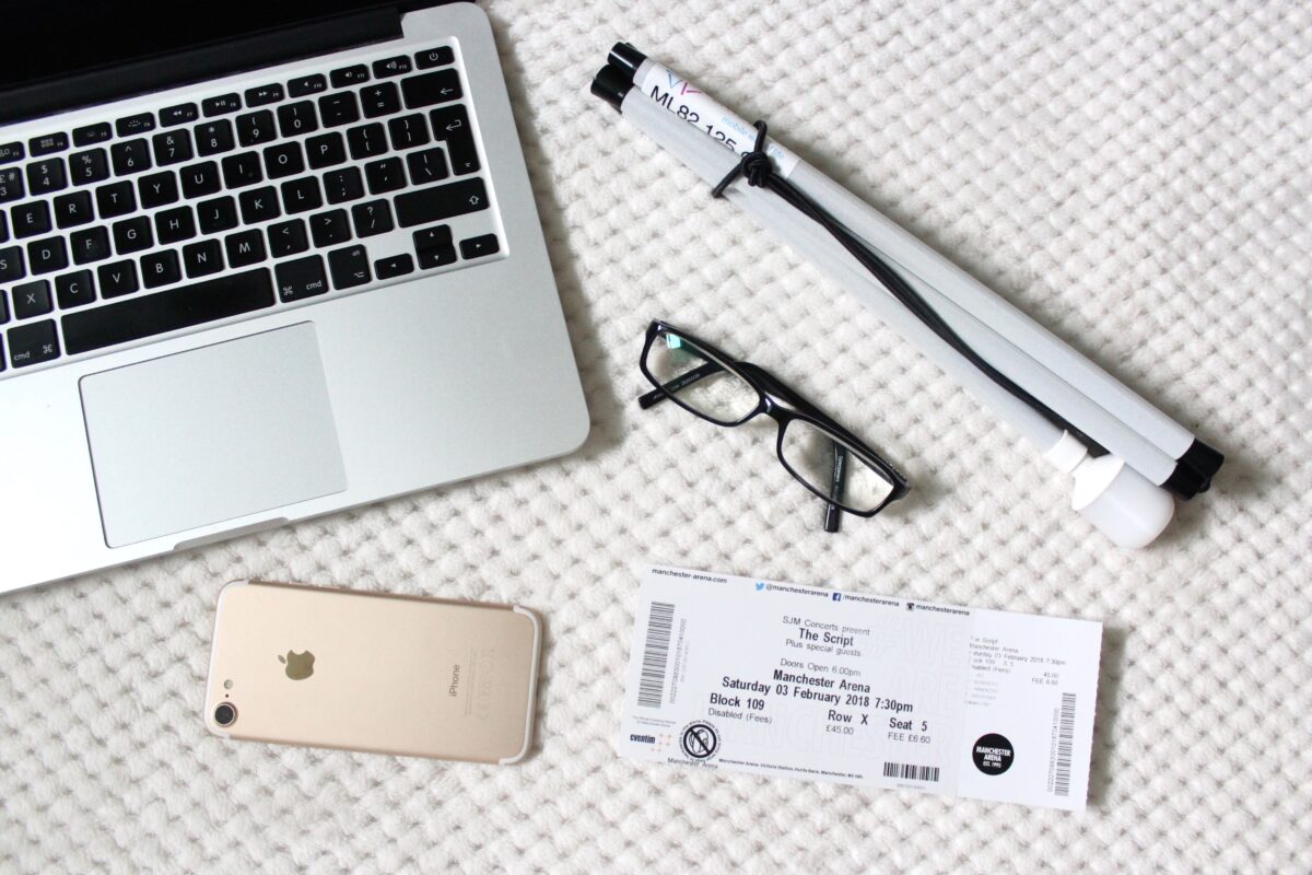 A photo of my macbook, iphone, a concert ticket, black frame glasses and my cane