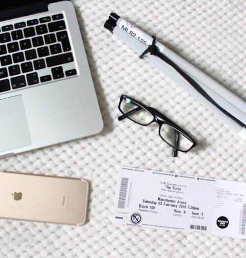 A photo of my macbook, iphone, a concert ticket, black frame glasses and my cane