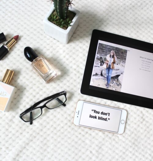 A photo of a phrase on my phone which says 'you don't look blind,; there is a pair of black glasses beside it and a couple of perfumes