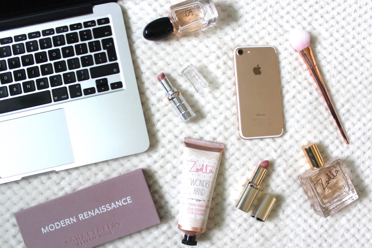 A photo of a macbook, iPhone and miscellaneous beauty products