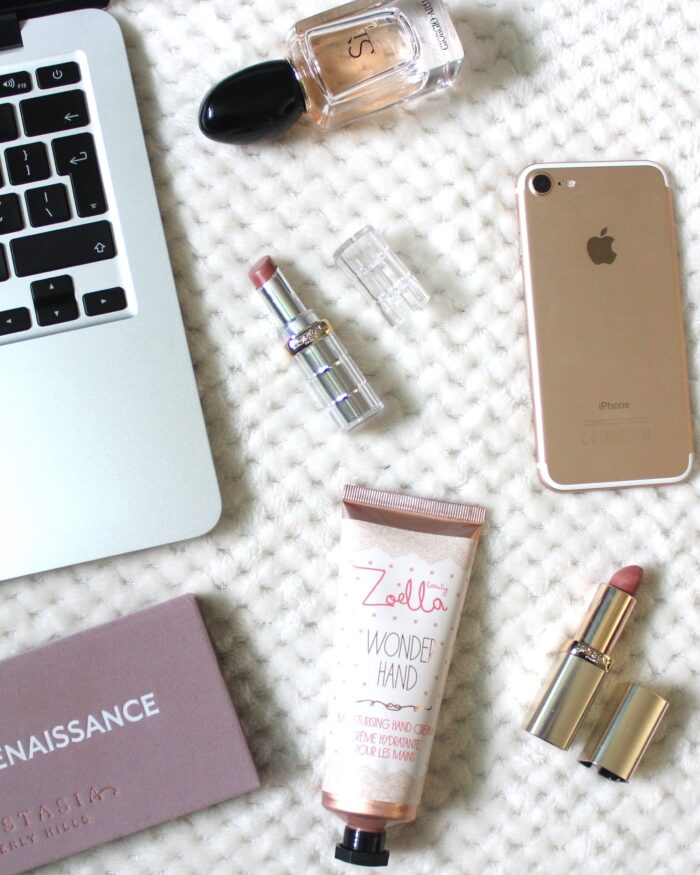A photo of a macbook, iPhone and miscellaneous beauty products