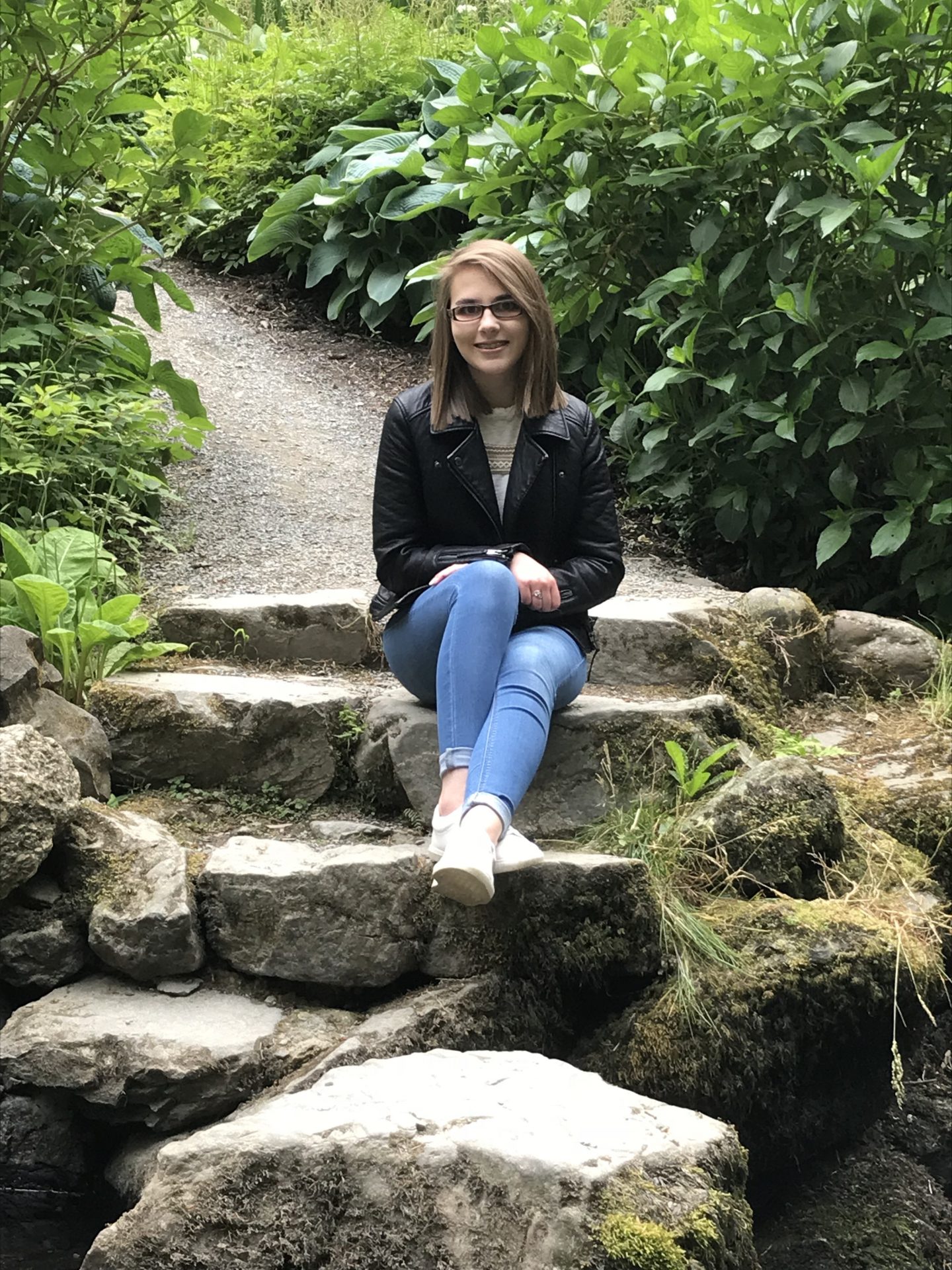A photo of Elin who has short brown hair, sitting on steps which lead down to some stepping stones