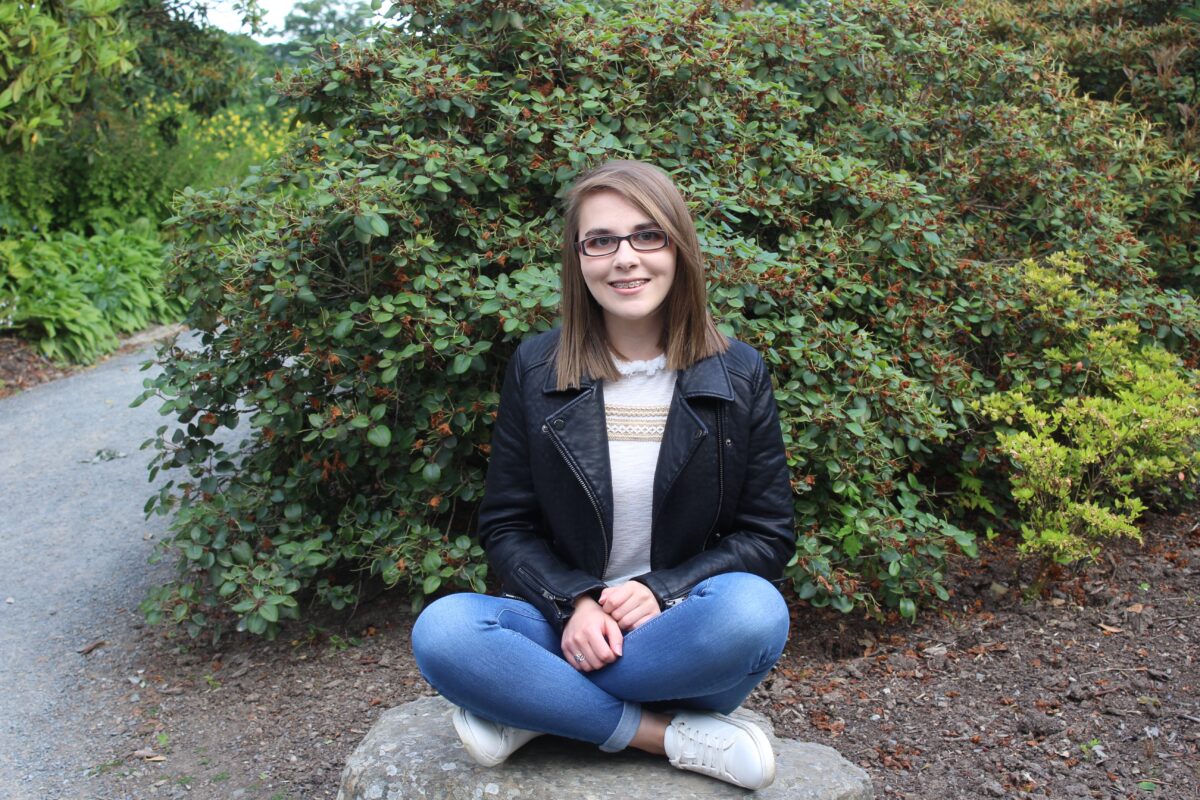 A photo of Elin sitting cross-legged on a rock with flowers in the background