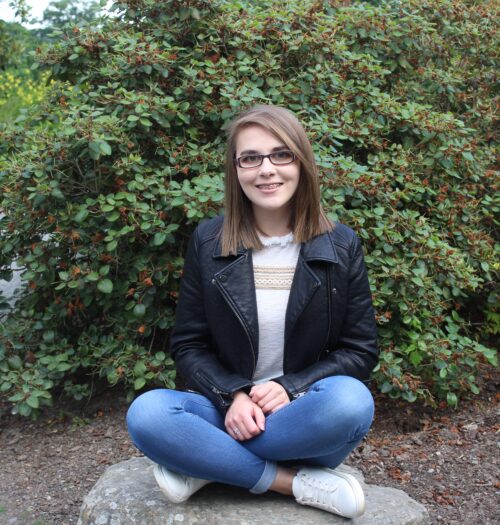 A photo of Elin sitting cross-legged on a rock with flowers in the background