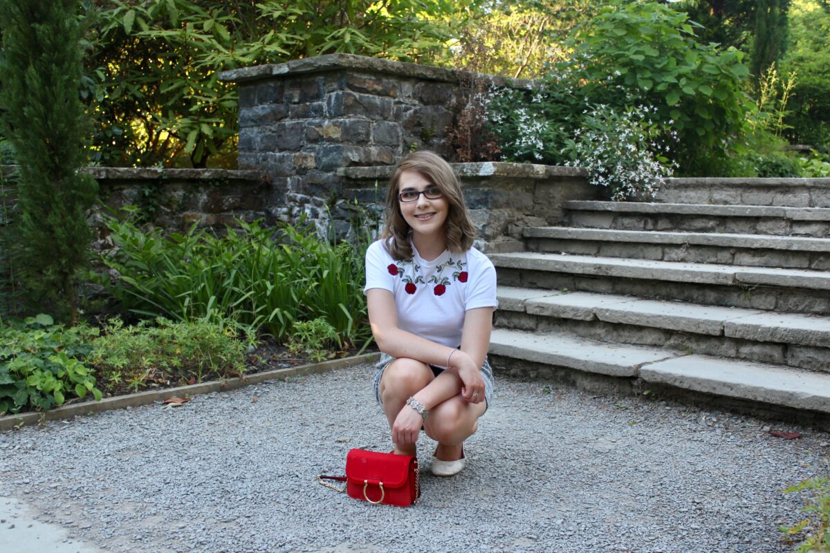 A photo of Elin crouching down in front of light steps, a red handbag with gold ring detail is in front of her