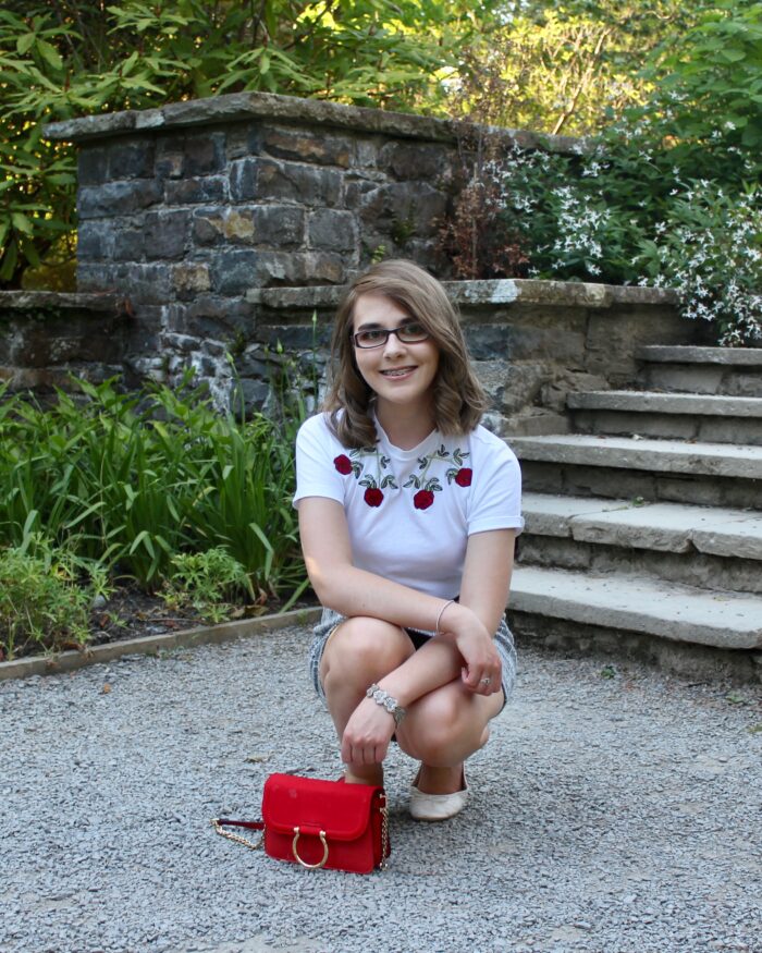 A photo of Elin crouching down in front of light steps, a red handbag with gold ring detail is in front of her