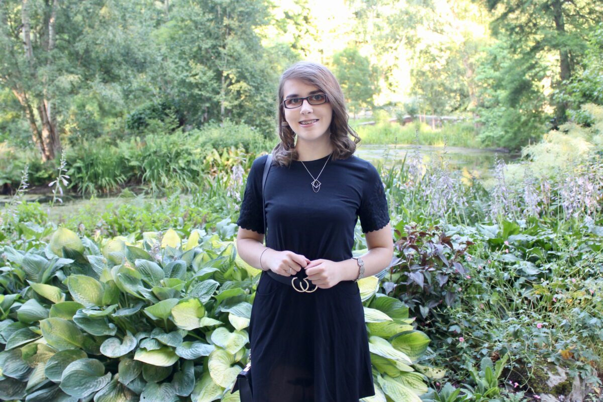 A photo of Elin wearing a black top and skirt with black and gold double circle belt