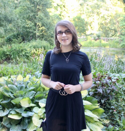 A photo of Elin wearing a black top and skirt with black and gold double circle belt