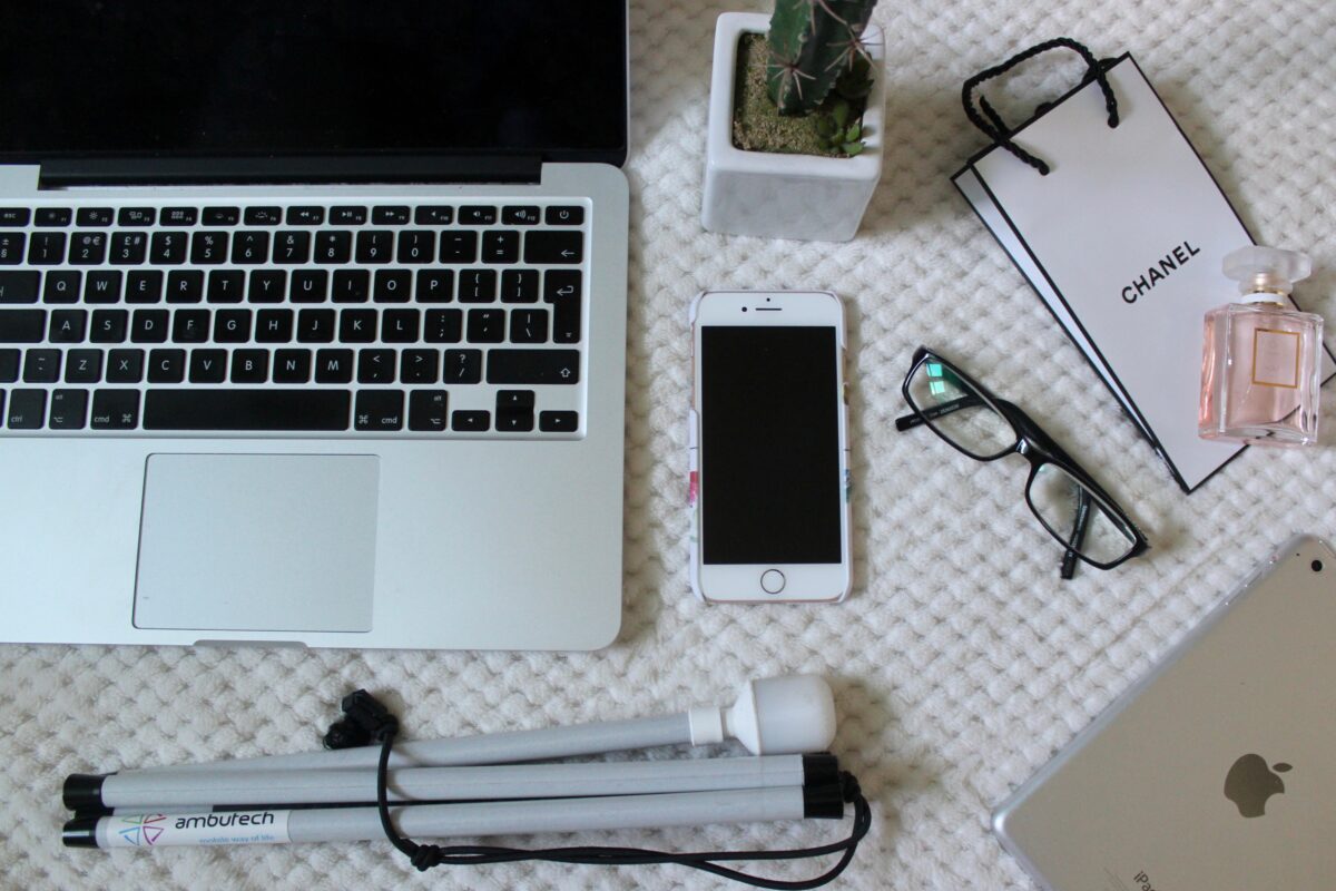 A photo of a macbook, white cane, iphone and ipad