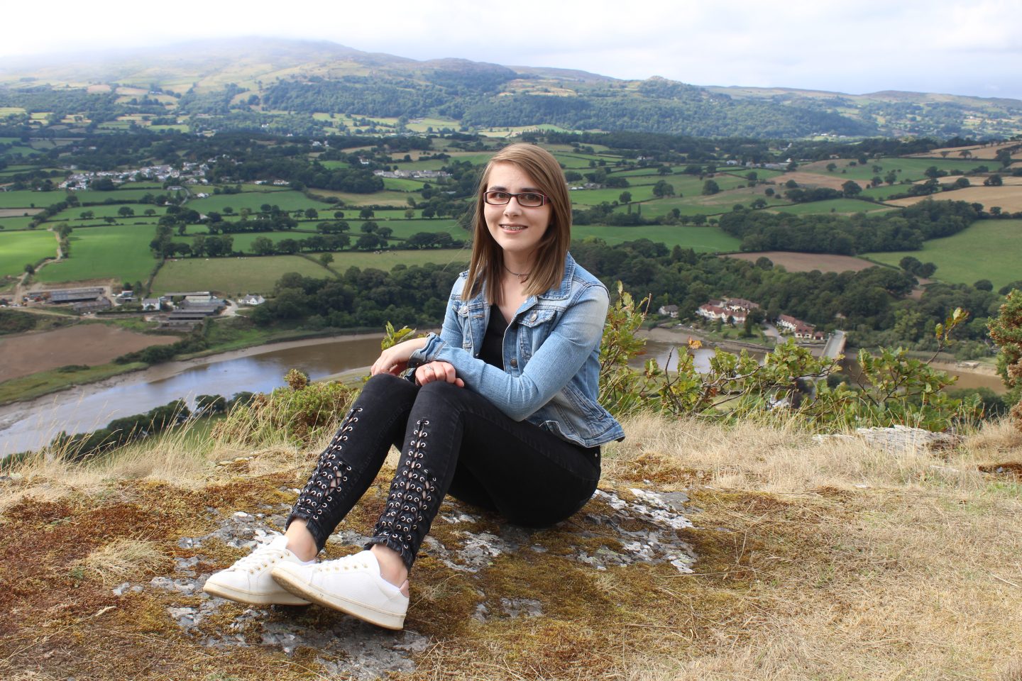 A photo of Elin sitting down with a river and mountains in the background