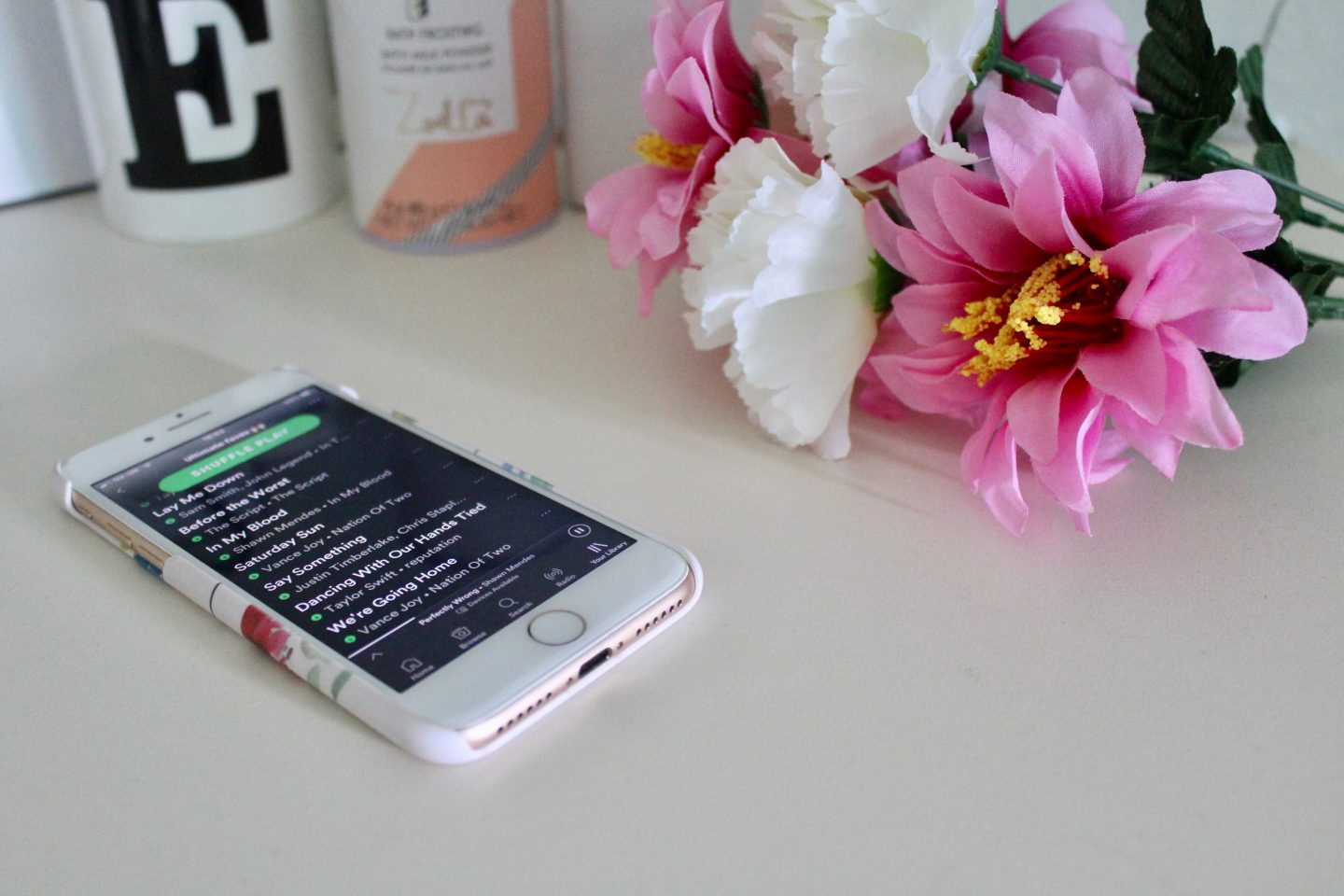 A photo of my spotify playlist on my phone with pink and white flowers next to it