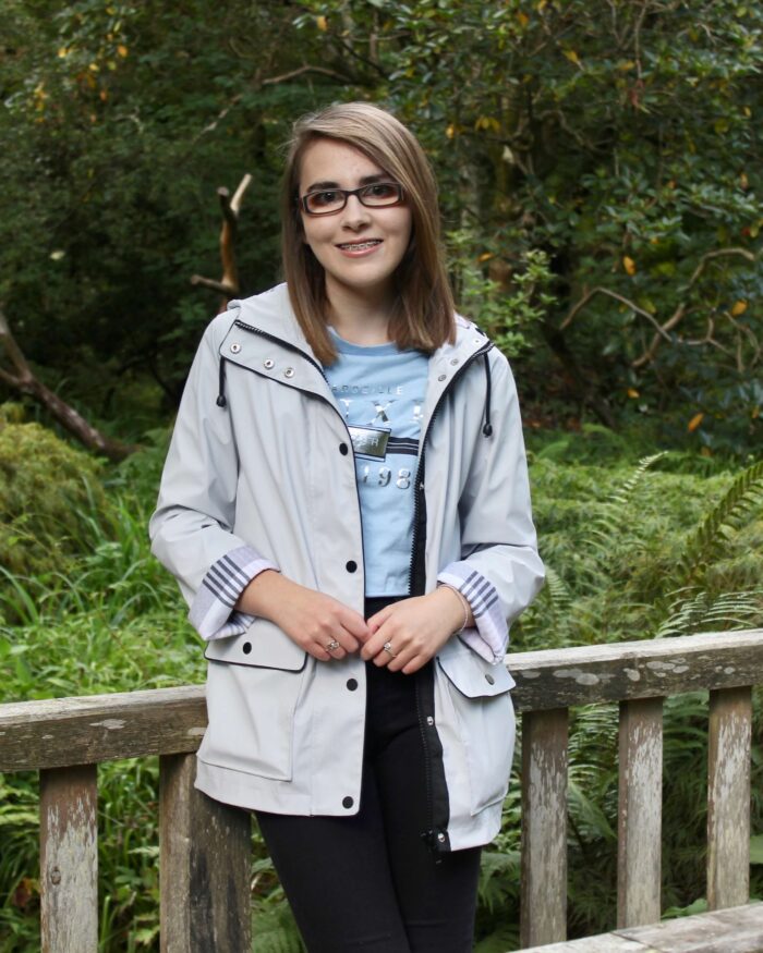 A photo of Elin in a grey raincoat standing on a wooden bridge