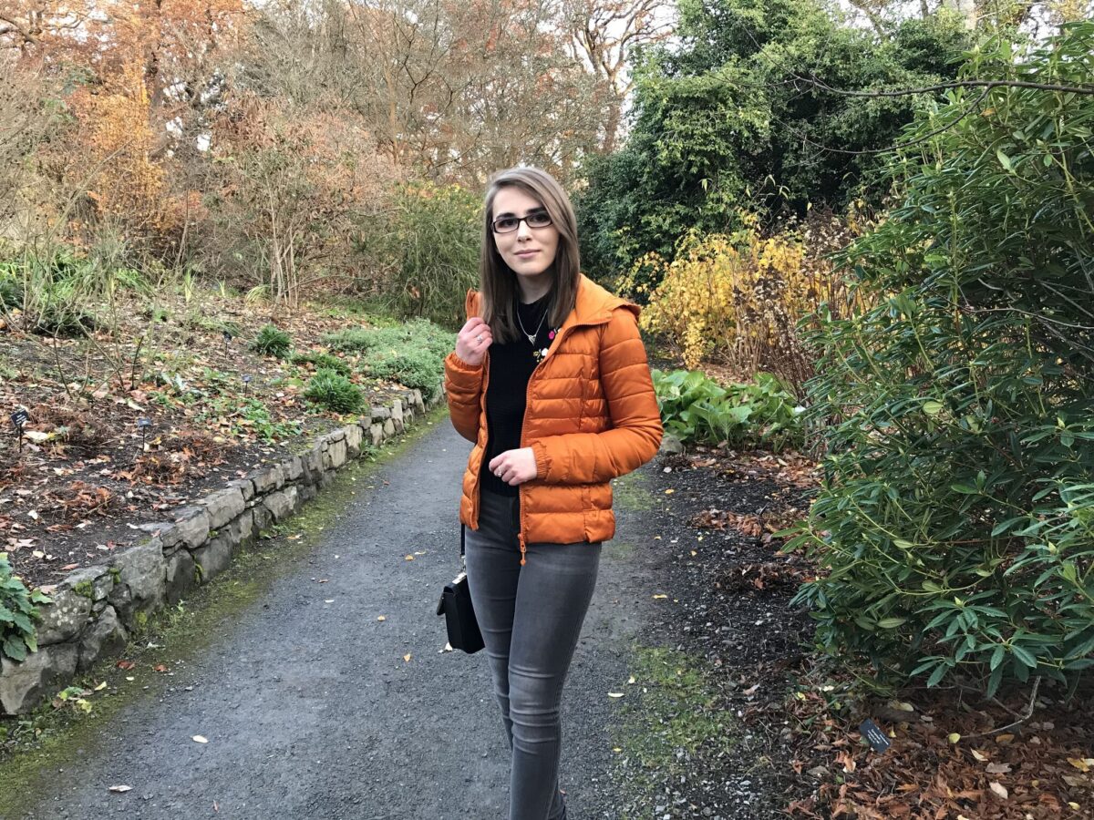 A photo of Elin on a path which has colourful plants and flowers and both sides