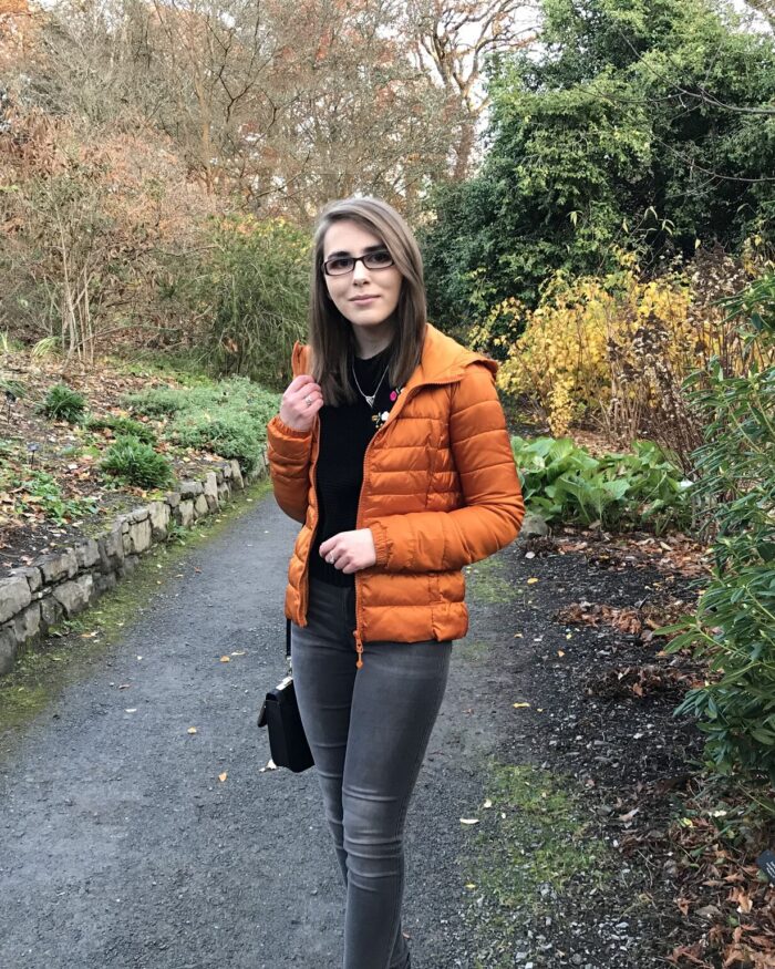 A photo of Elin on a path which has colourful plants and flowers and both sides