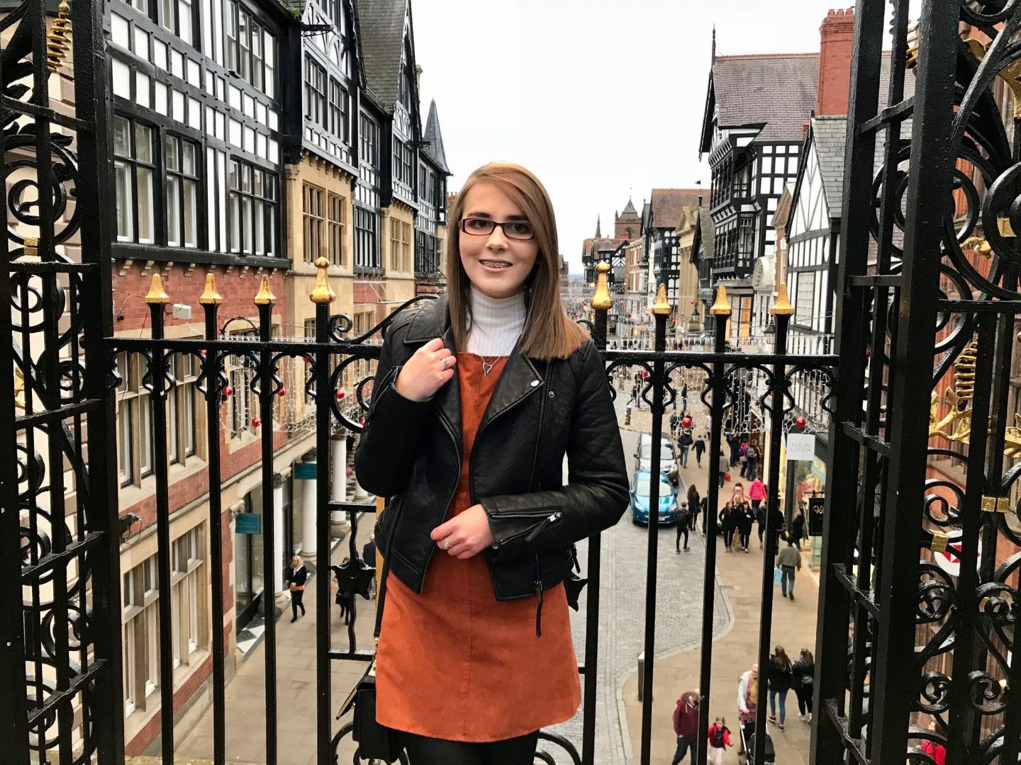 A photo of Elin in front of black railings, a street in Chester is shown in the background