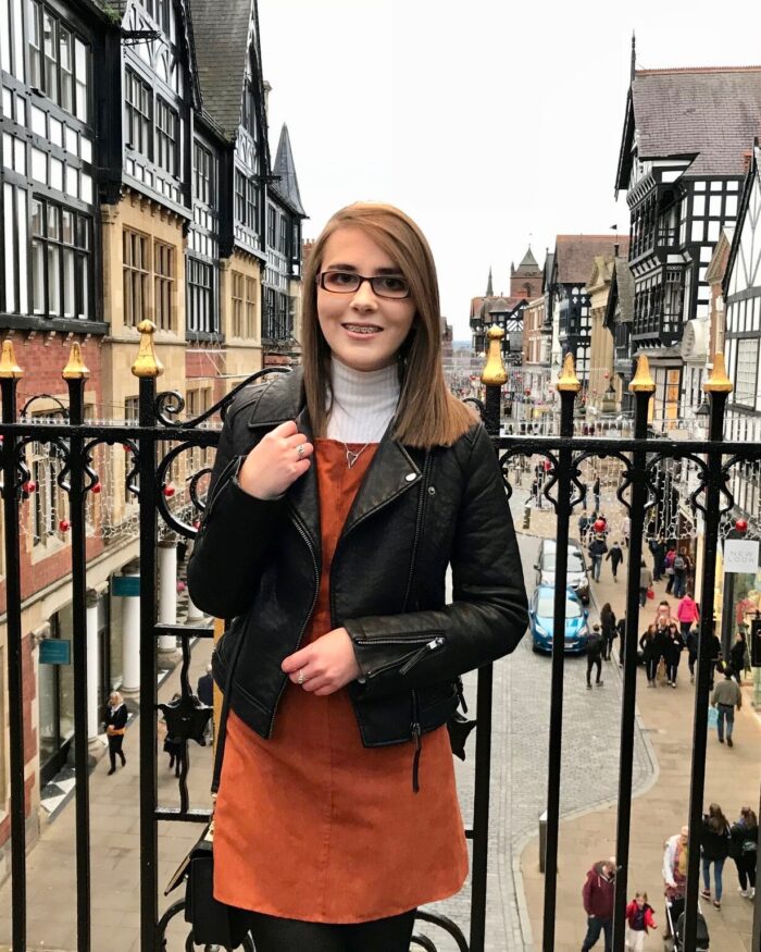 A photo of Elin in front of black railings, a street in Chester is shown in the background