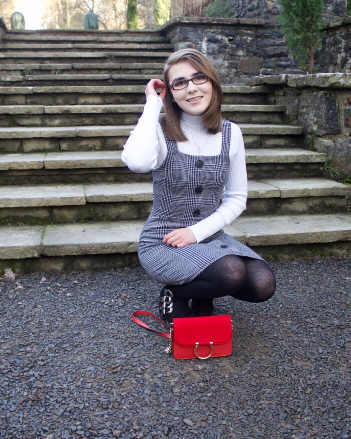 A photo of Elin crouching down in front of some light steps, her red handbag is place upright on the floor in front of her