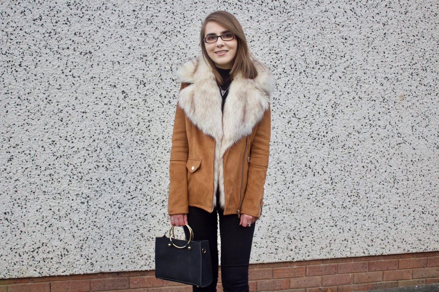 A photo of Elin wearing a brown faux suede jacket, black high neck top and black skinny jeans
