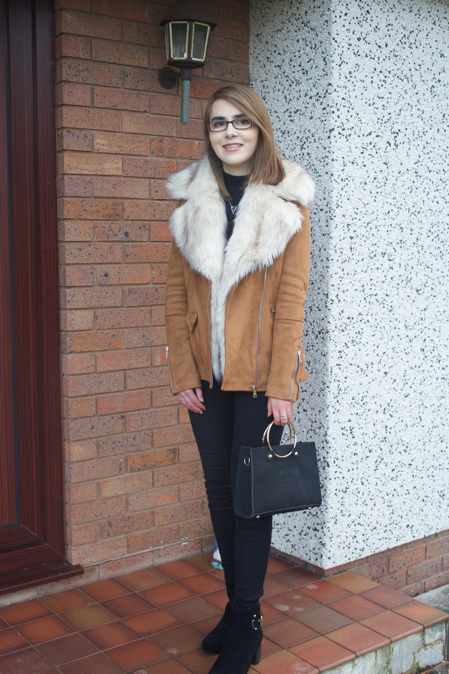 A photo showing Elin's full outfit which is a brown suede jacket with a faux fur collar, a black high neck top, black skinny jeans and heeled ankle boots.