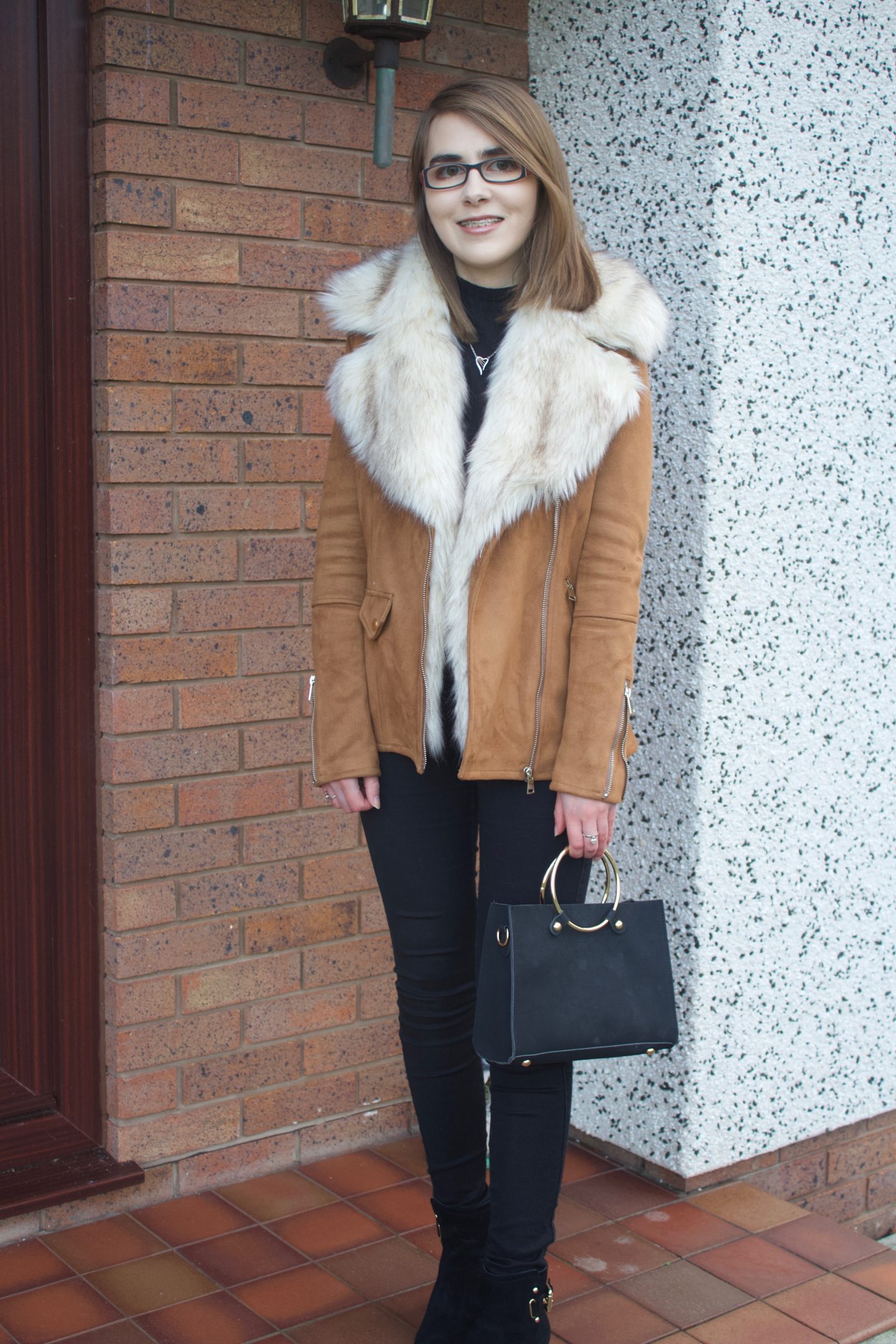 A photo showing Elin's full outfit which is a brown suede jacket with a faux fur collar, a black high neck top, black skinny jeans and heeled ankle boots.