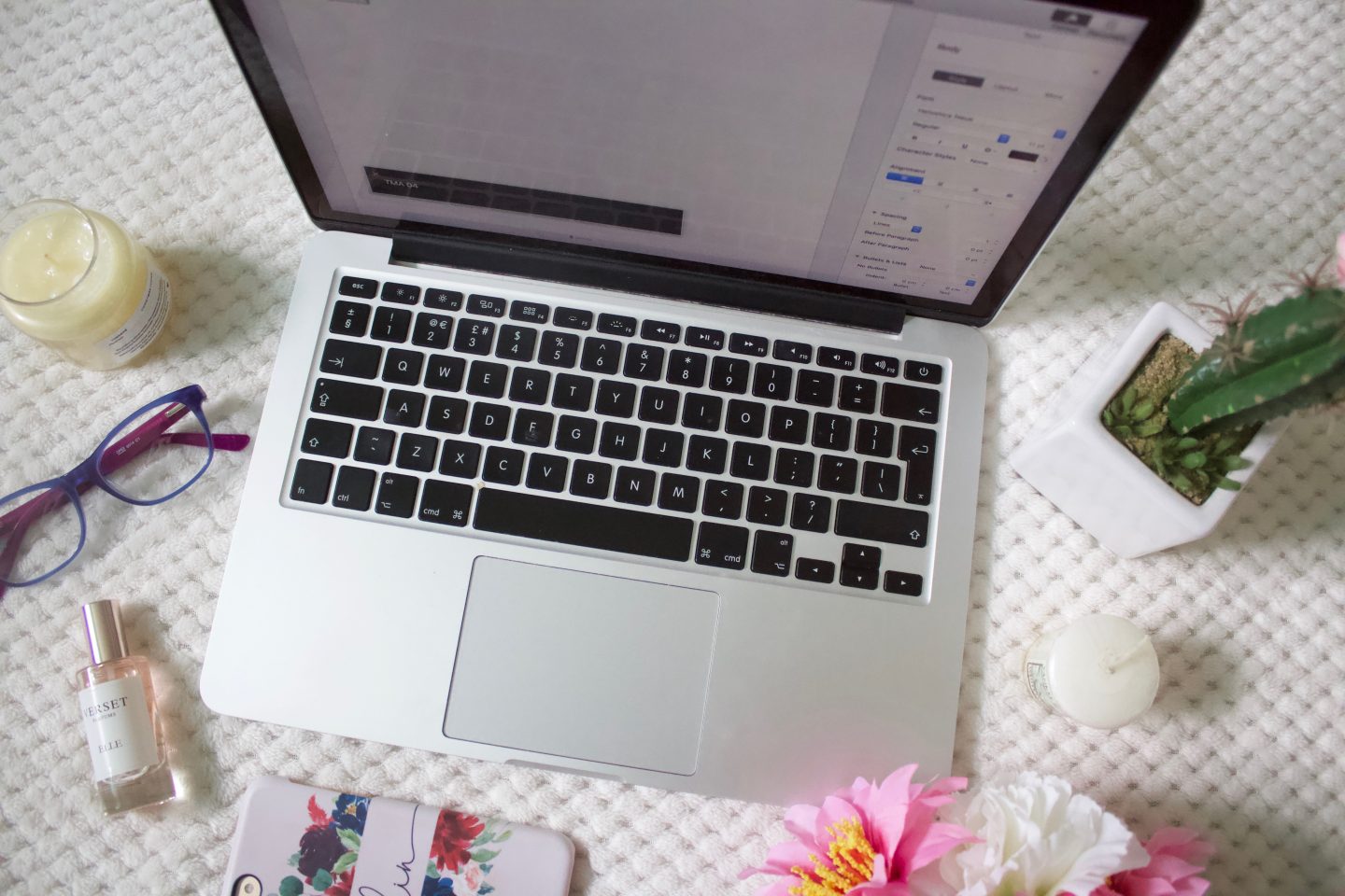 A photo of a document which is open on my macbook, there are some items around the mac - two candles, fake flowers, a fake cactus, my phone, a pair of glasses and a small perfume