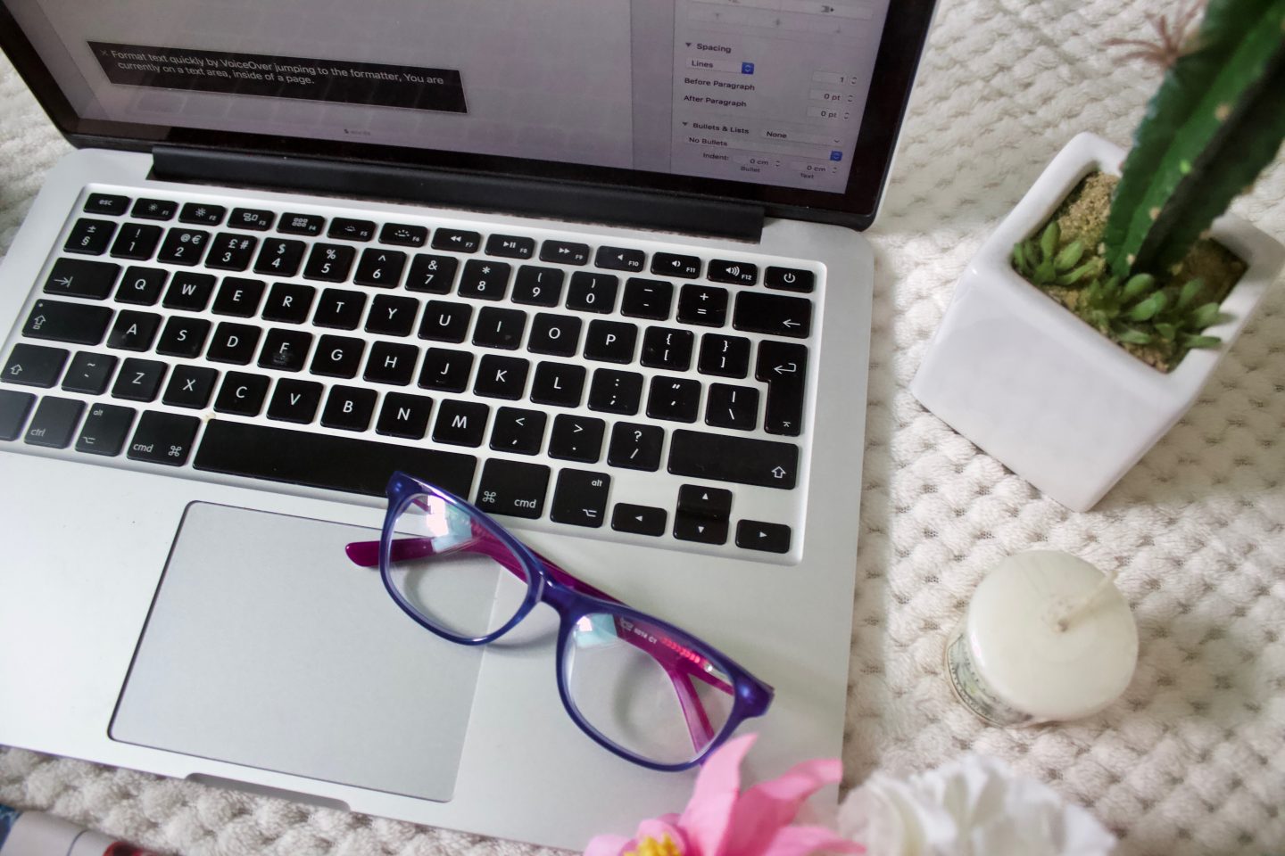 A photo of a pair of glasses placed on a macbook keyboard, there is a small yankee candle and a fake cactus beside it