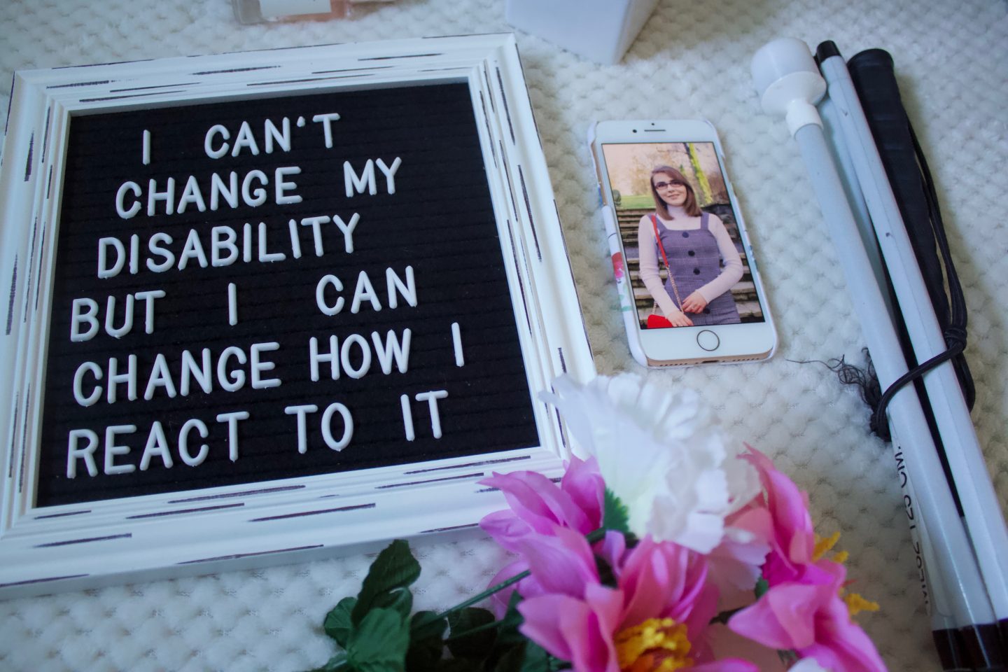 A photo of a felt letter board with the writing 'I can't change my disability but I can change how I react to it', my phone is beside it with a photo of me showing and my white cane is beside that.