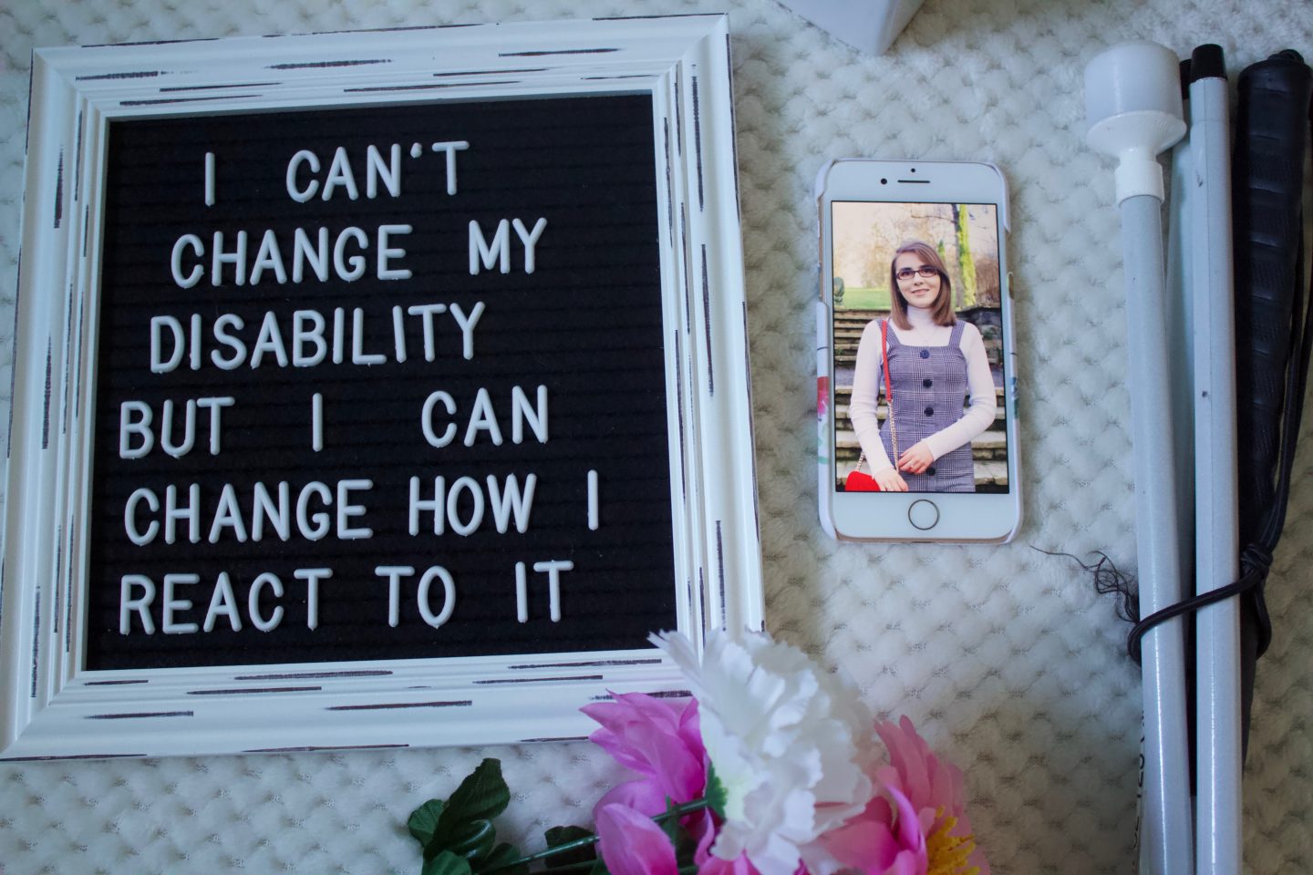 A photo of a felt letter board with the writing 'I can't change my disability but I can change how I react to it', my phone is beside it with a photo of me showing and my white cane is beside that.