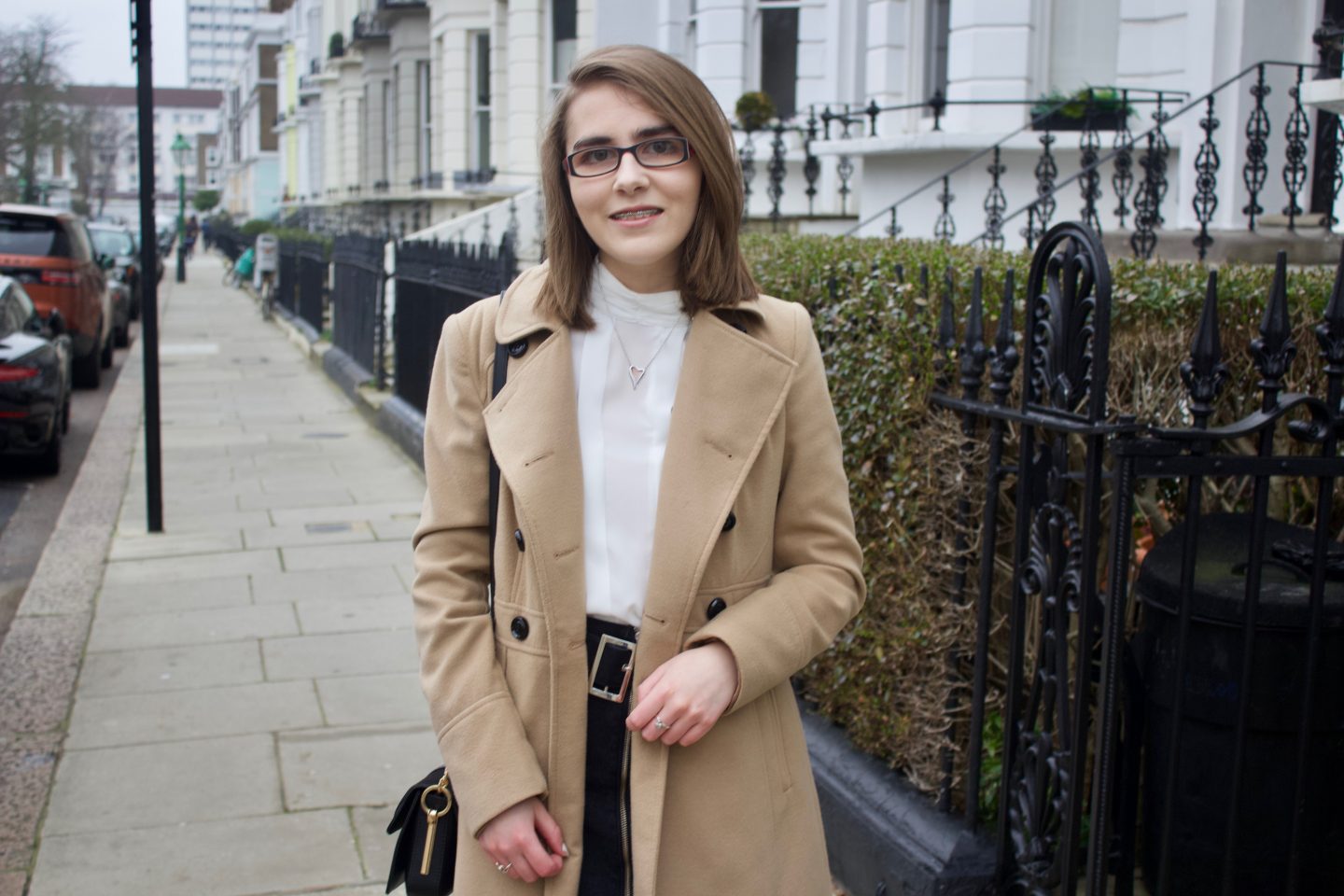 Elin standing on a street with white houses and black railings on the right hand side