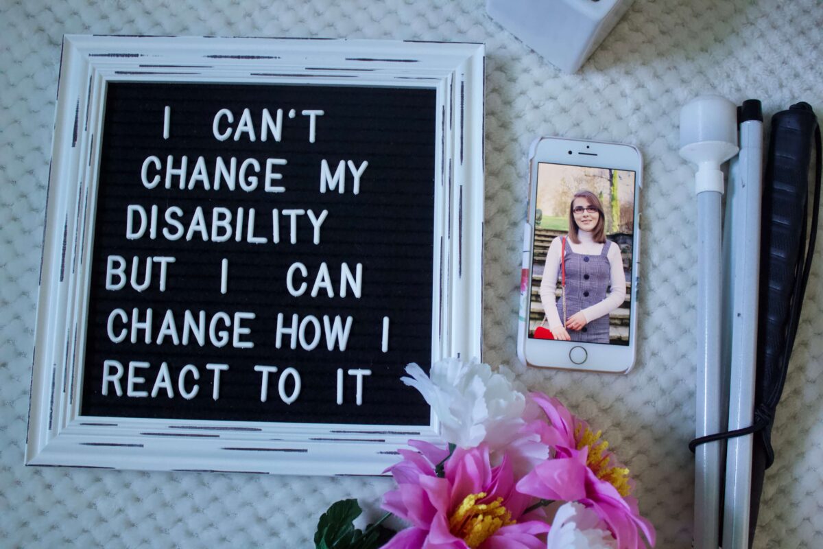 A photo of a felt letter board with the writing 'I can't change my disability but I can change how I react to it', my phone is beside it with a photo of me showing and my white cane is beside that.