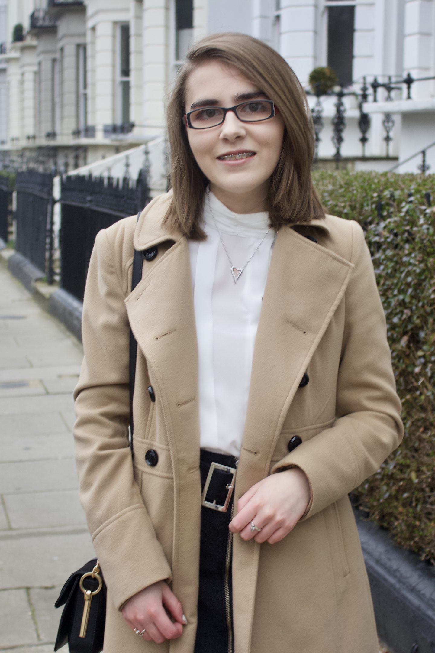 Elin standing on a street with white houses and black railings on the right hand side