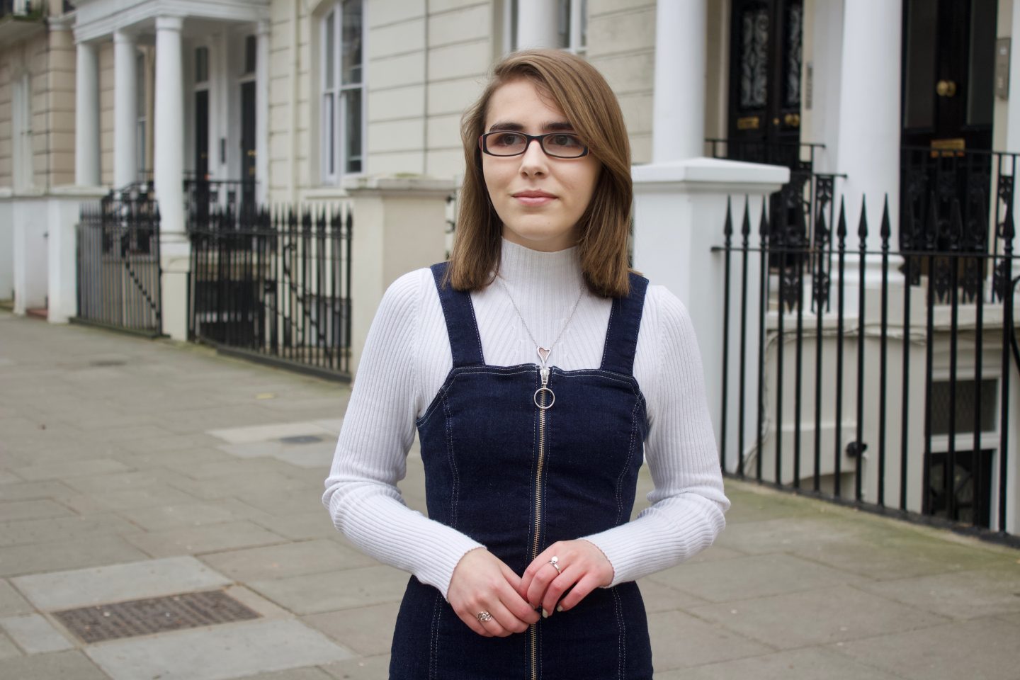 A photo of Elin looking away from the camera, a white house with black railings in front of it can be seen in the background