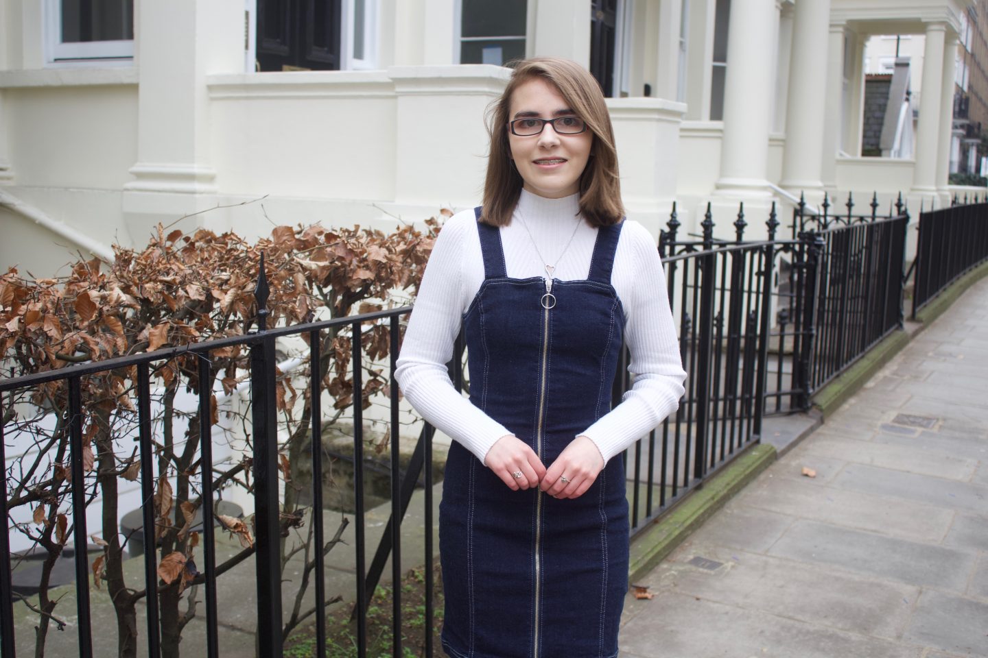 A photo of Elin standing in front of black railings which has pink flowers along the top