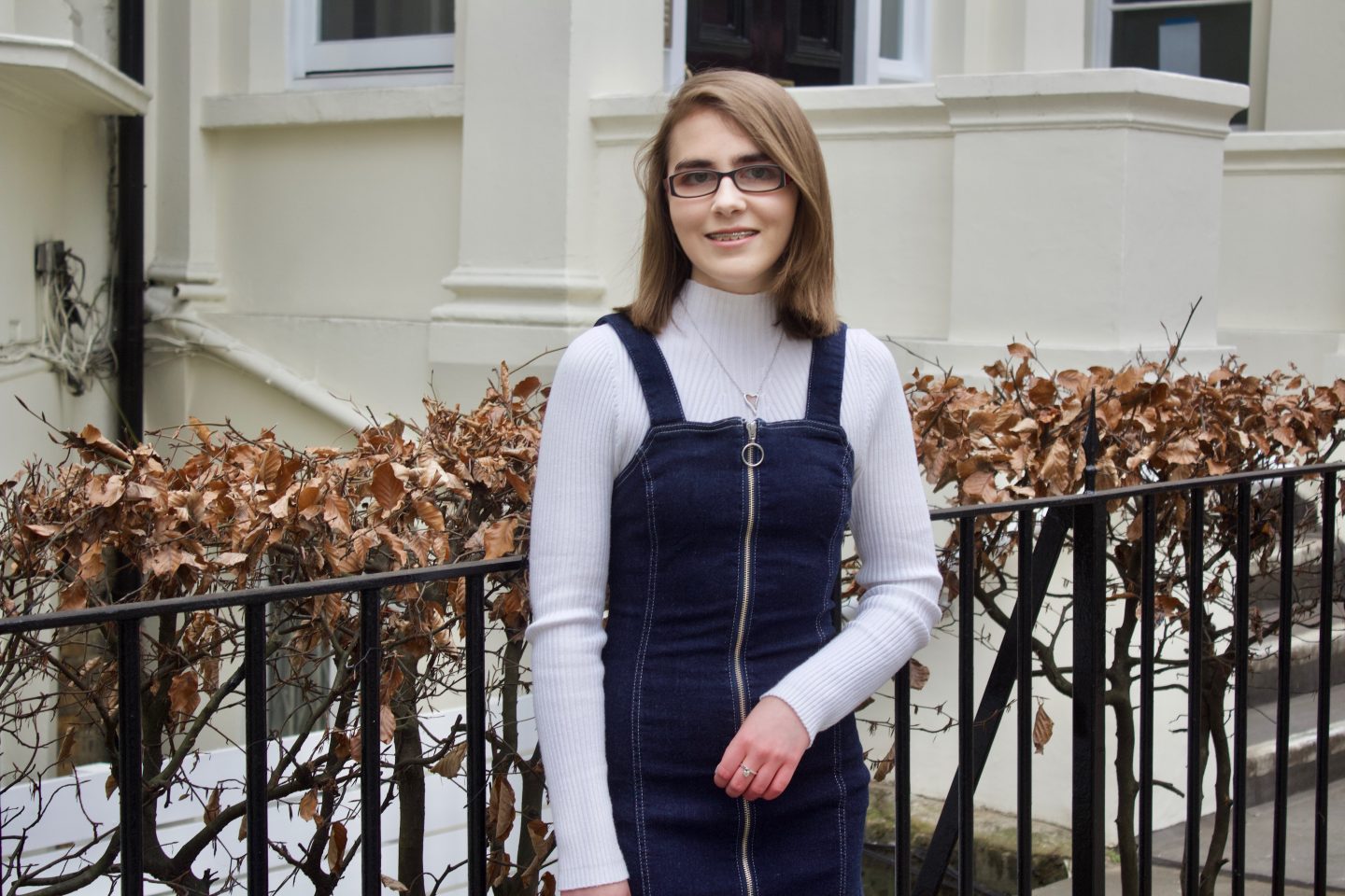 My struggle with confidence: A photo of Elin standing in front of black railings which has pink flowers along the top