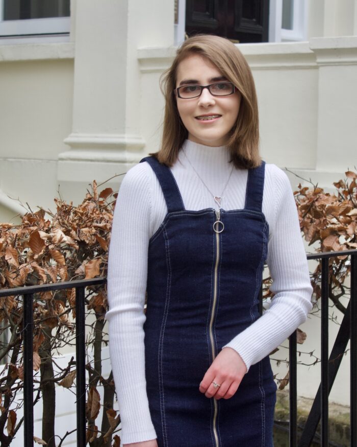 A photo of Elin standing in front of black railings which has pink flowers along the top