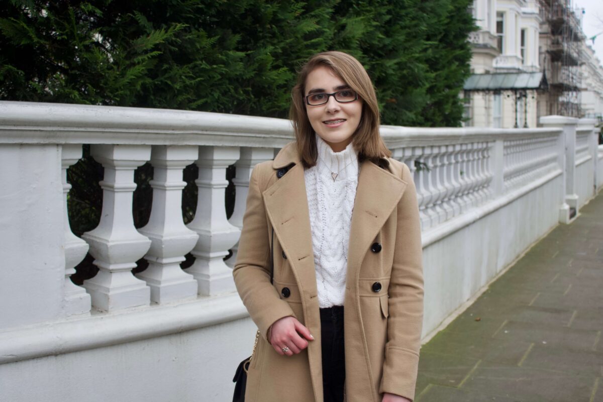 A photo of Elin in front of a pretty white fence with trees in the background