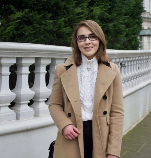A photo of Elin in front of a pretty white fence with trees in the background