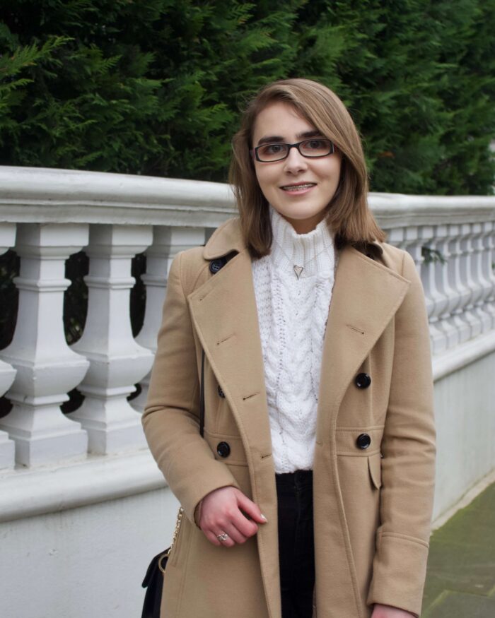 A photo of Elin in front of a pretty white fence with trees in the background