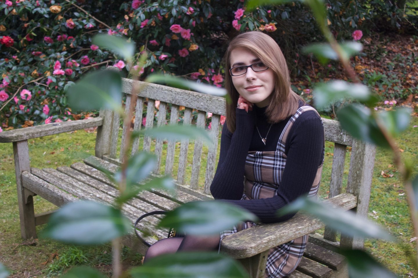 A photo of Elin sitting on a bench with flowers in front and behind her