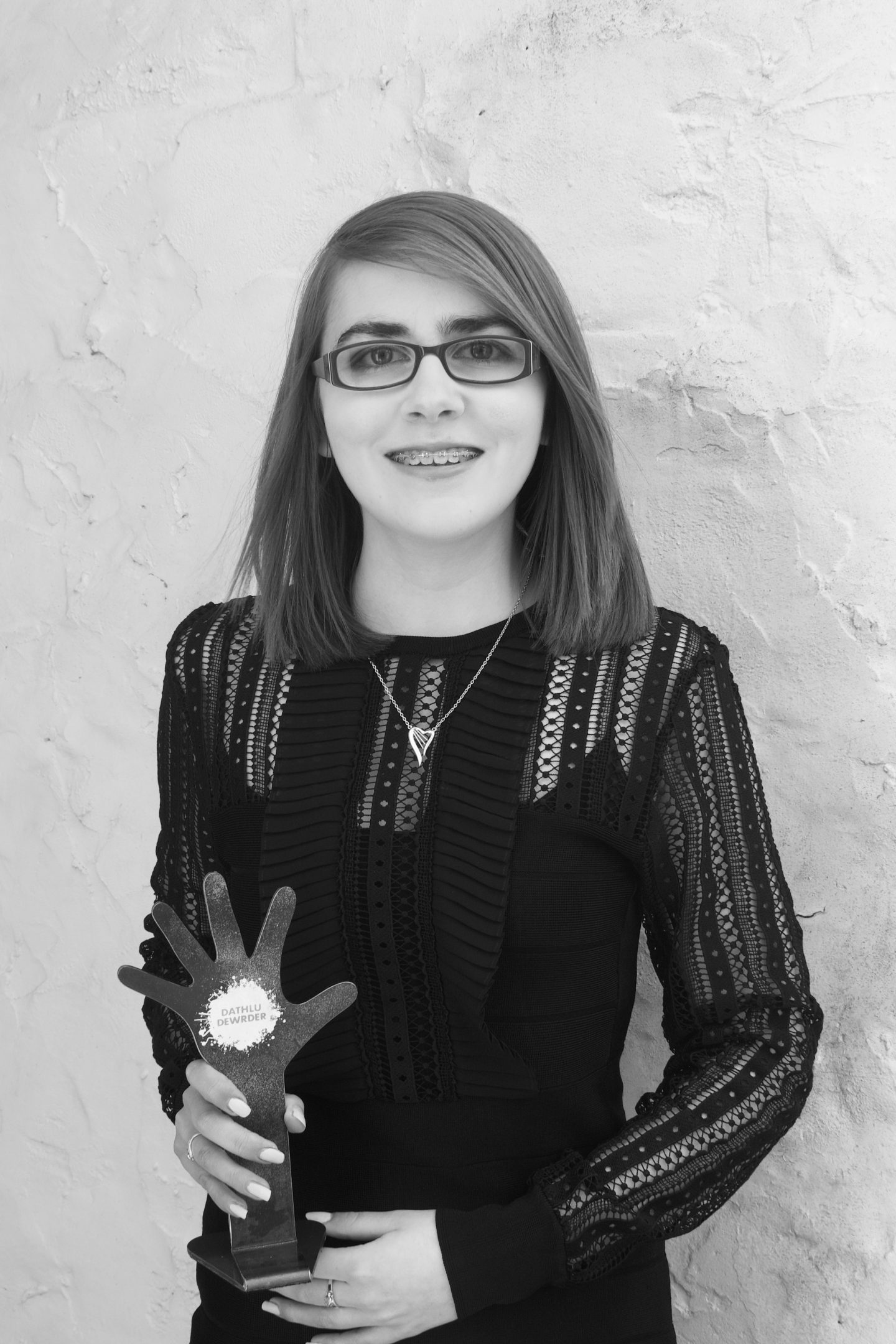 A photo of Elin holding her 'Dathlu Dewrder' award which is in a shape of a hand being raised