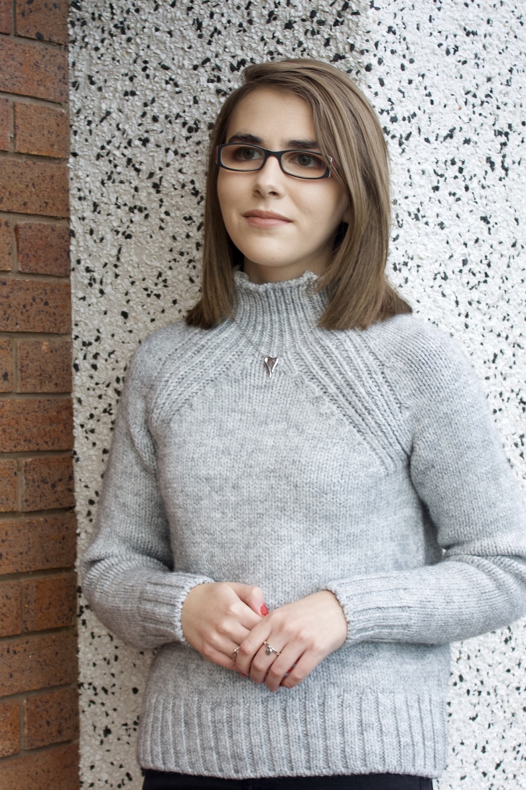 A photo of Elin wearing a light grey high neck jumper, she is looking away from the camera