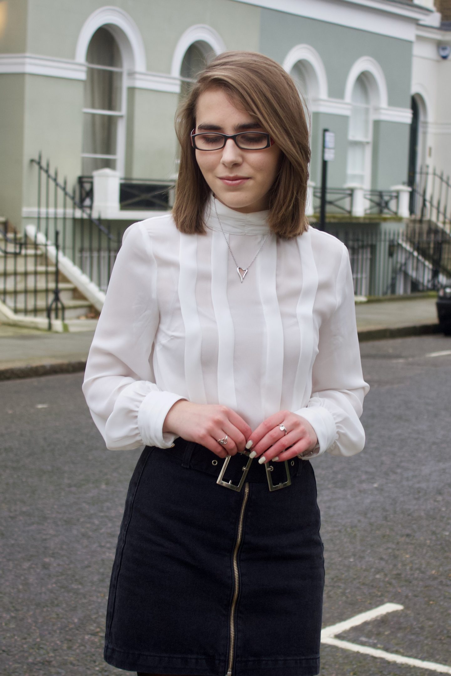 A photo of Elin looking down, she is standing on a street in London and there are houses in the background