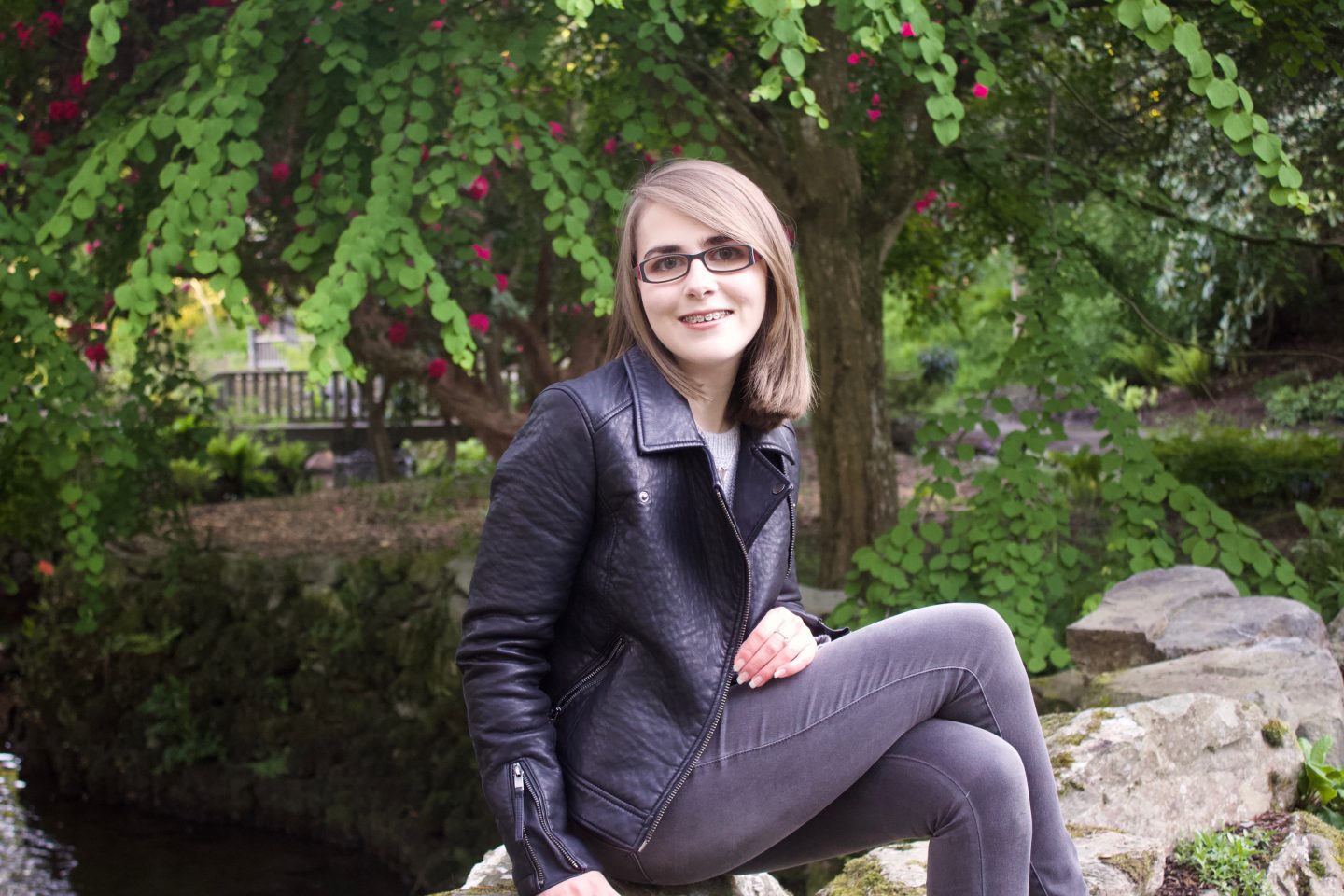 A photo of Elin sitting on a rock with greenery in the background
