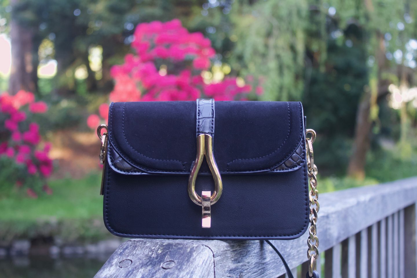 A photo of a black cross body bag with a gold buckle on the front